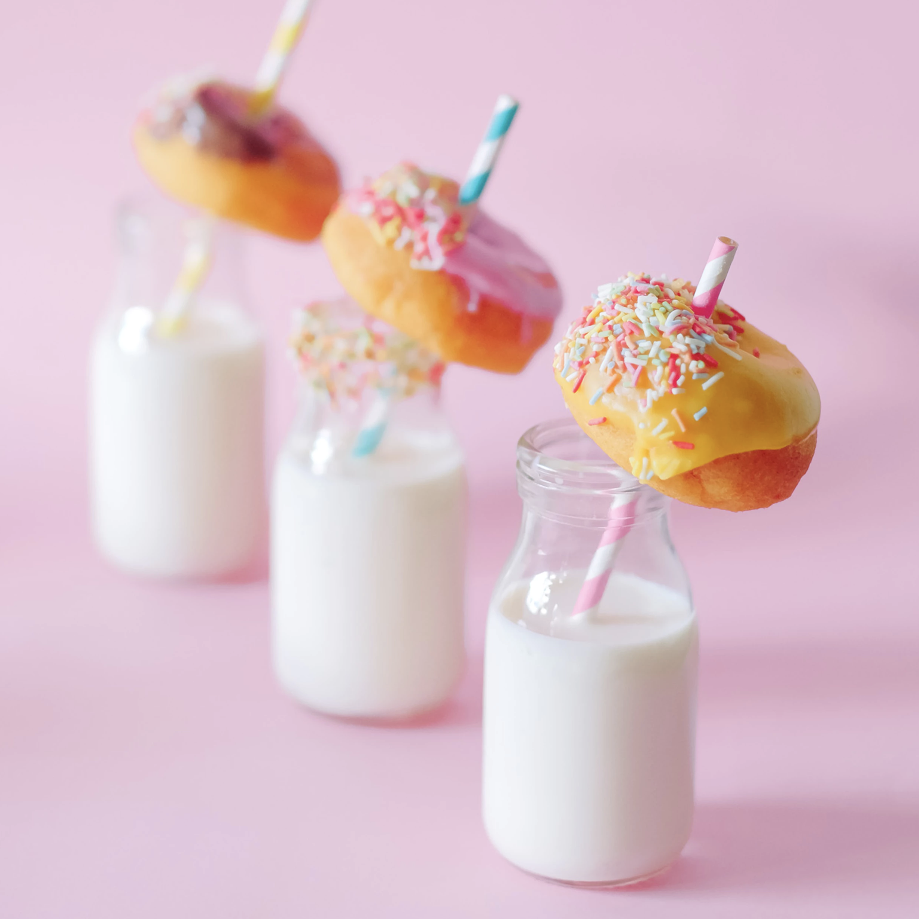 Three bottles of milk with donuts on the straws